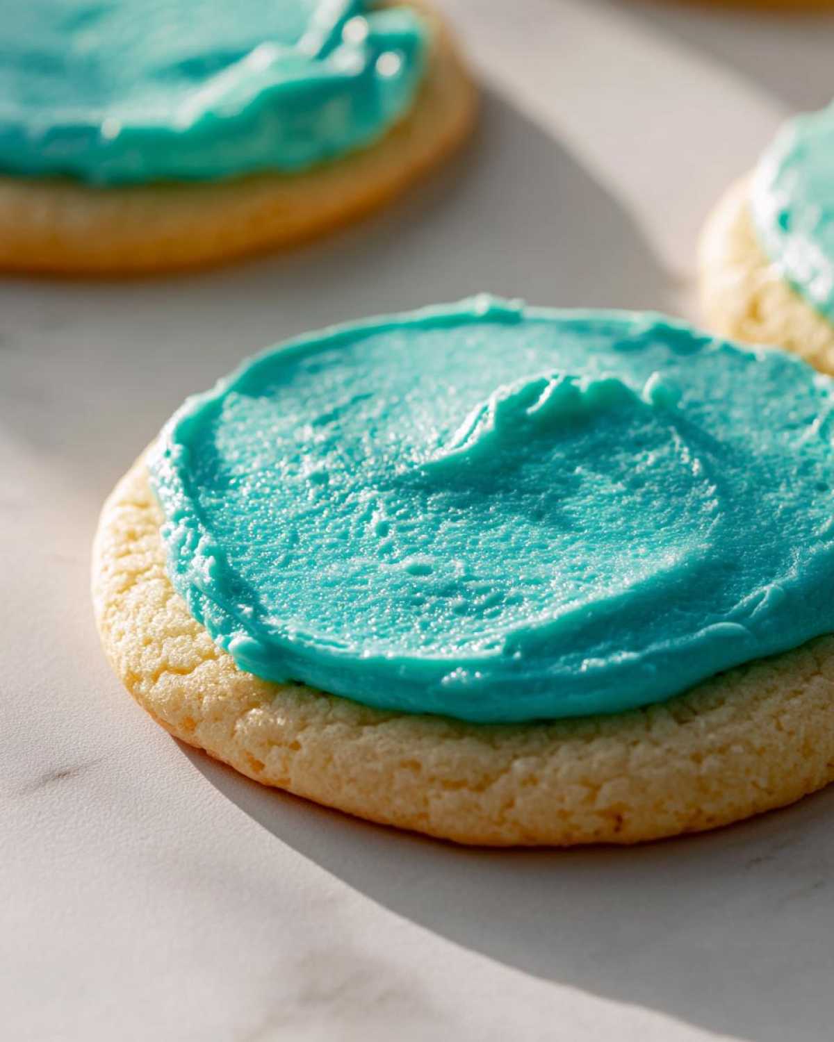 A close-up of a soft sugar cookie topped with thick, bright turquoise sugar cookie icing recipe.