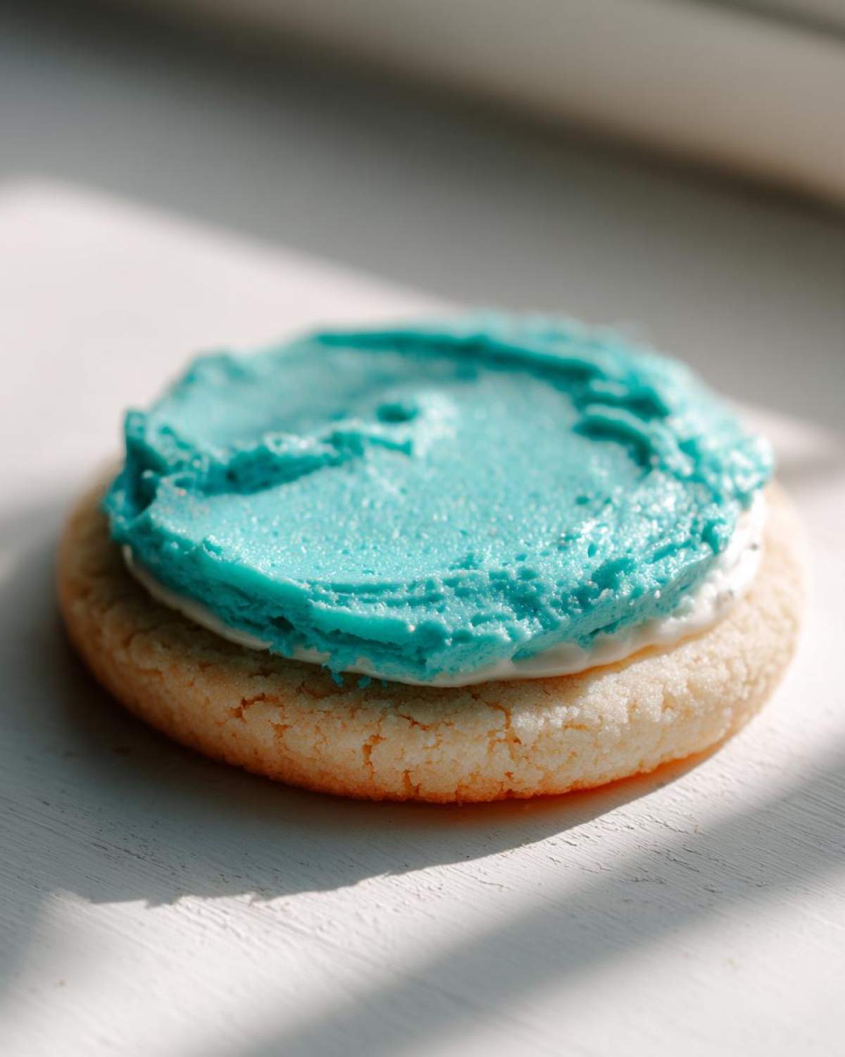 A single sugar cookie topped with a thick layer of bright blue sugar cookie icing recipe.