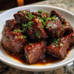 Close-up of tender crockpot steak bites coated in a glossy, dark sauce and garnished with fresh parsley.