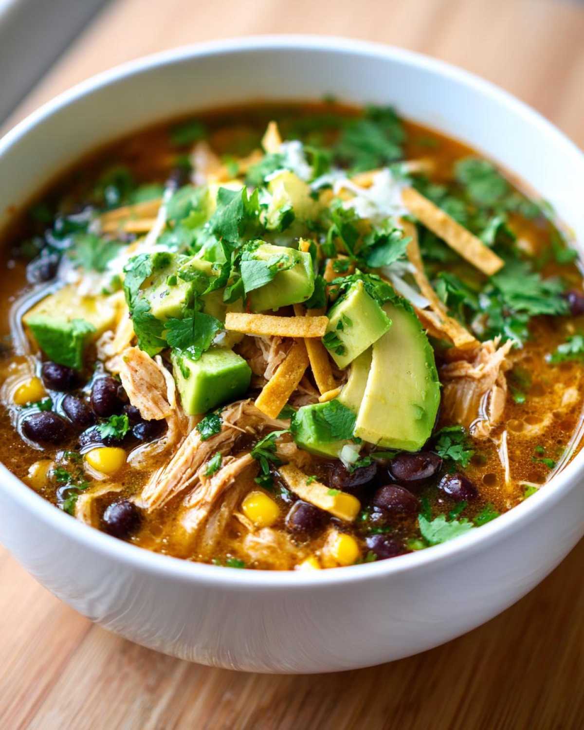 Close-up of a bowl of tortilla soup recipe topped with avocado, cilantro, and tortilla strips.