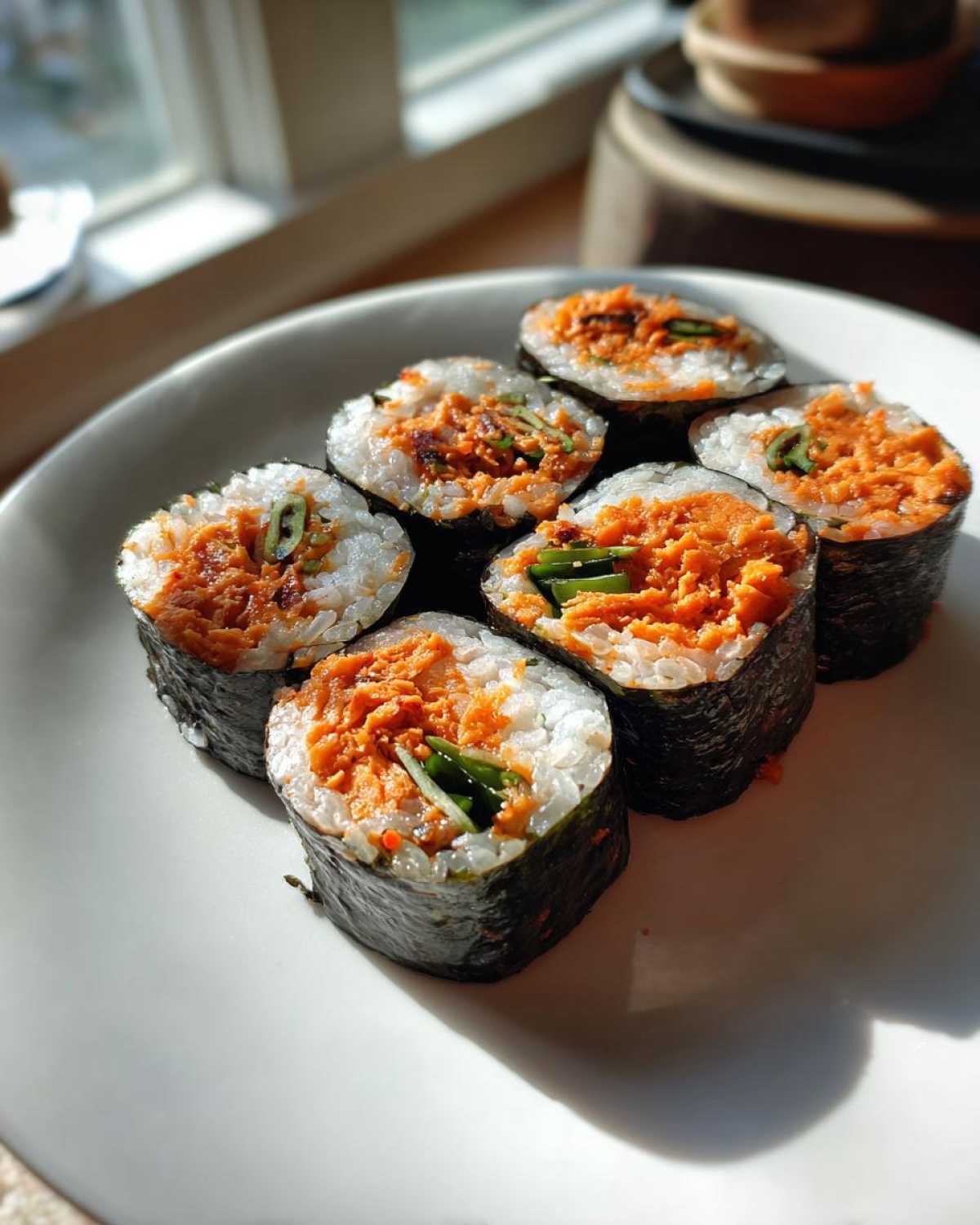 Six slices of vibrant tuna kimbap filled with spicy orange filling and green scallions, arranged on a white plate.