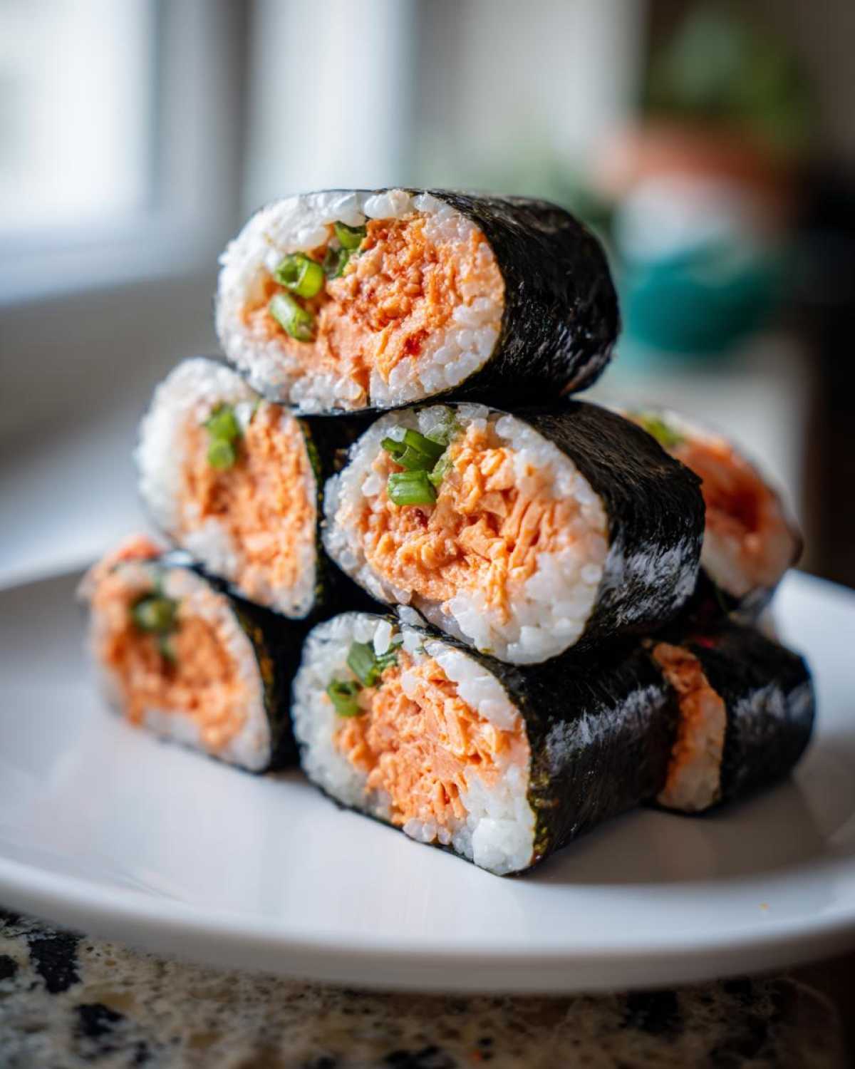 A stack of six freshly cut pieces of tuna kimbap, featuring orange spicy tuna filling and green onions, resting on a white plate.