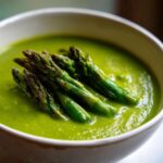 Close-up of vibrant green asparagus soup topped with roasted asparagus spears.