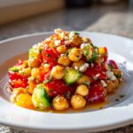 Close-up of a vibrant mediterranean chickpea salad featuring tomatoes, cucumbers, and crumbled feta cheese.
