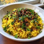 A close-up of vibrant yellow mediterranean rice topped with toasted pine nuts and fresh chopped parsley.