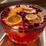 Close-up of a festive non-alcoholic Christmas punch garnished with orange slices and fresh cranberries.
