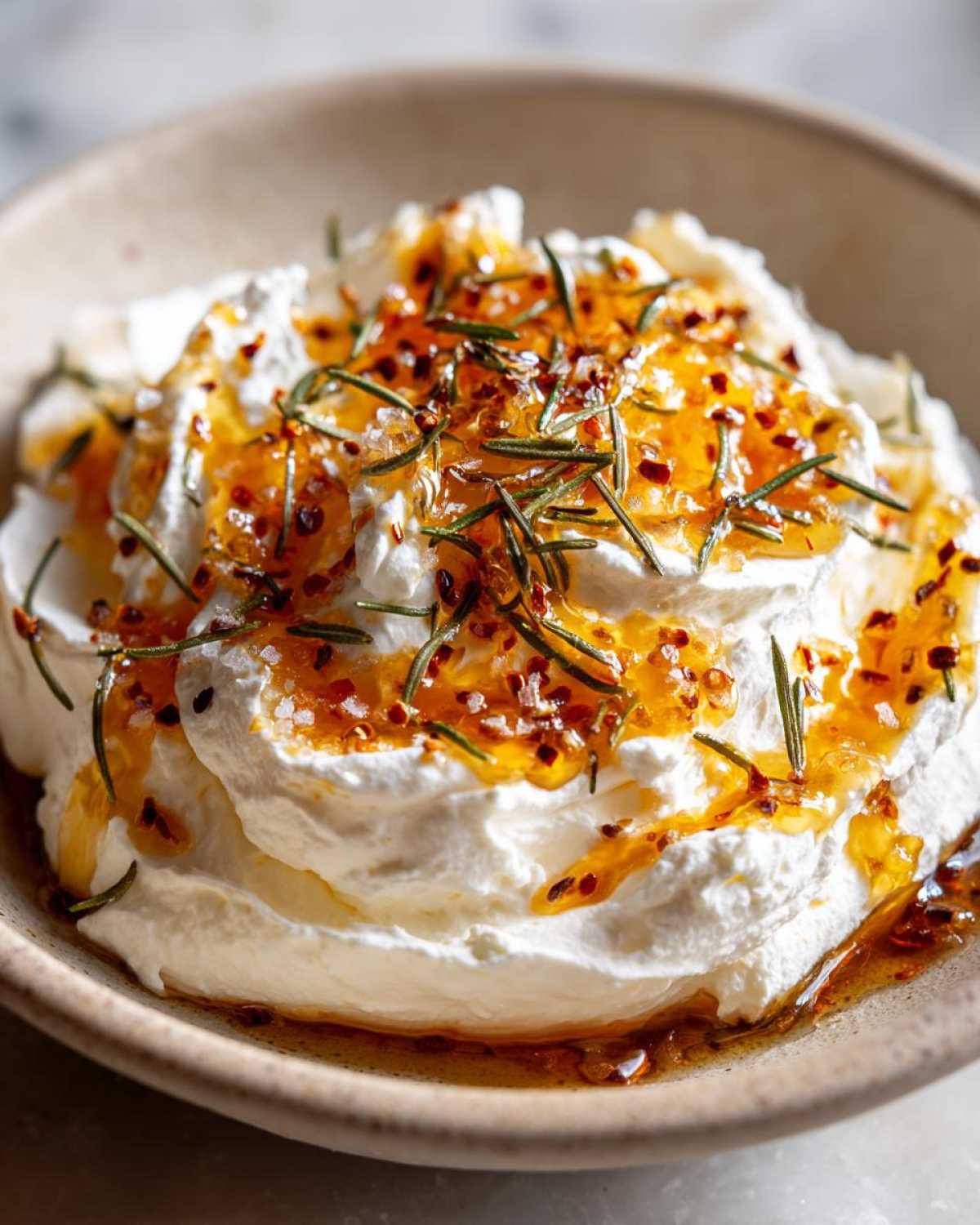 Close-up of creamy whipped ricotta dip drizzled with hot honey, chili flakes, and fresh rosemary sprigs.