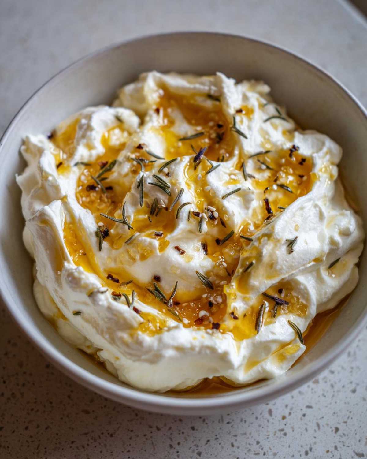 Close-up of creamy whipped ricotta dip drizzled with golden honey and topped with fresh rosemary sprigs.