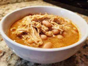 Close-up of a white bowl filled with creamy white chicken chili, featuring shredded white chicken and cannellini beans.