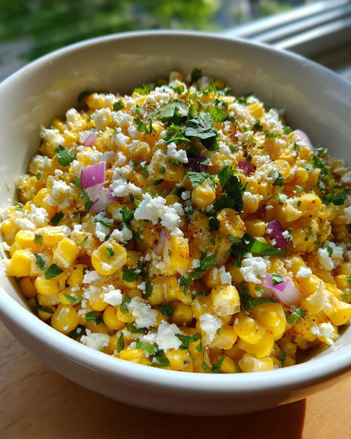 A close-up view of a vibrant street corn salad featuring yellow corn kernels, white cotija cheese, red onion, and cilantro.