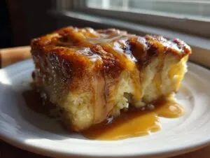 A rich, golden slice of bread pudding topped generously with dripping caramel sauce on a white plate.