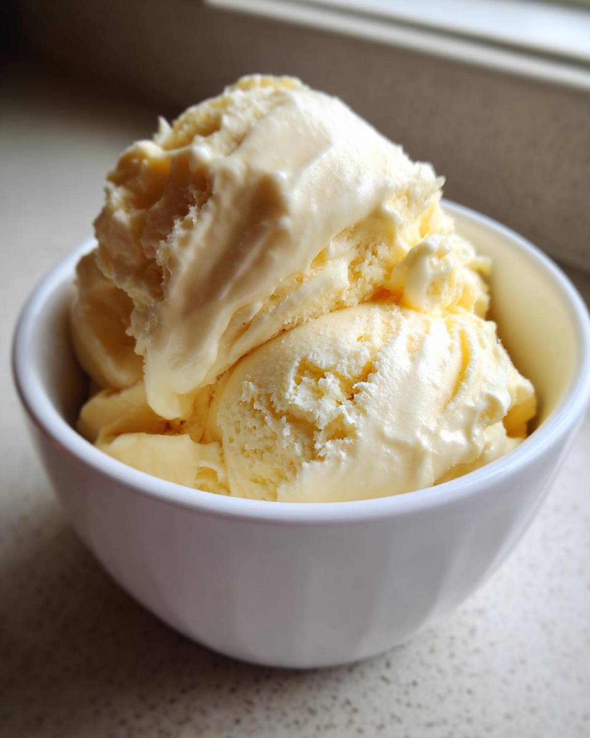 Close-up of creamy scoops of homemade banana ice cream melting slightly in a white bowl.
