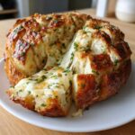 Close-up of a round loaf of pull-apart cheese bread with melted cheese stretching between the pieces.