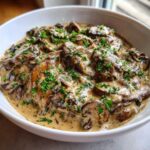 Close-up of a rich, creamy mushroom sauce loaded with sliced mushrooms and topped with fresh parsley.