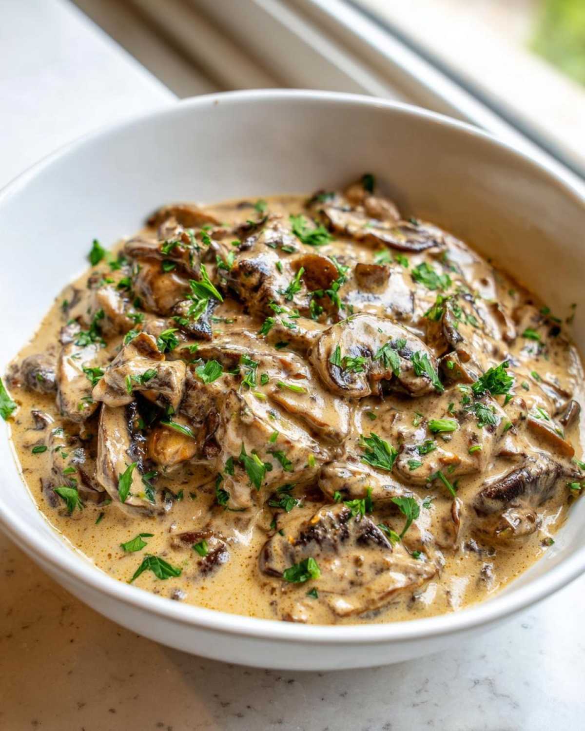 A close-up of rich, creamy mushroom sauce loaded with sliced mushrooms and topped with fresh parsley.