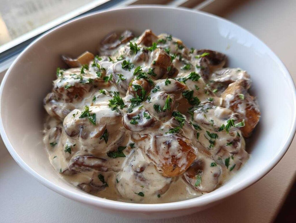 A close-up of a white bowl filled with rich, creamy mushroom sauce, garnished with fresh parsley.
