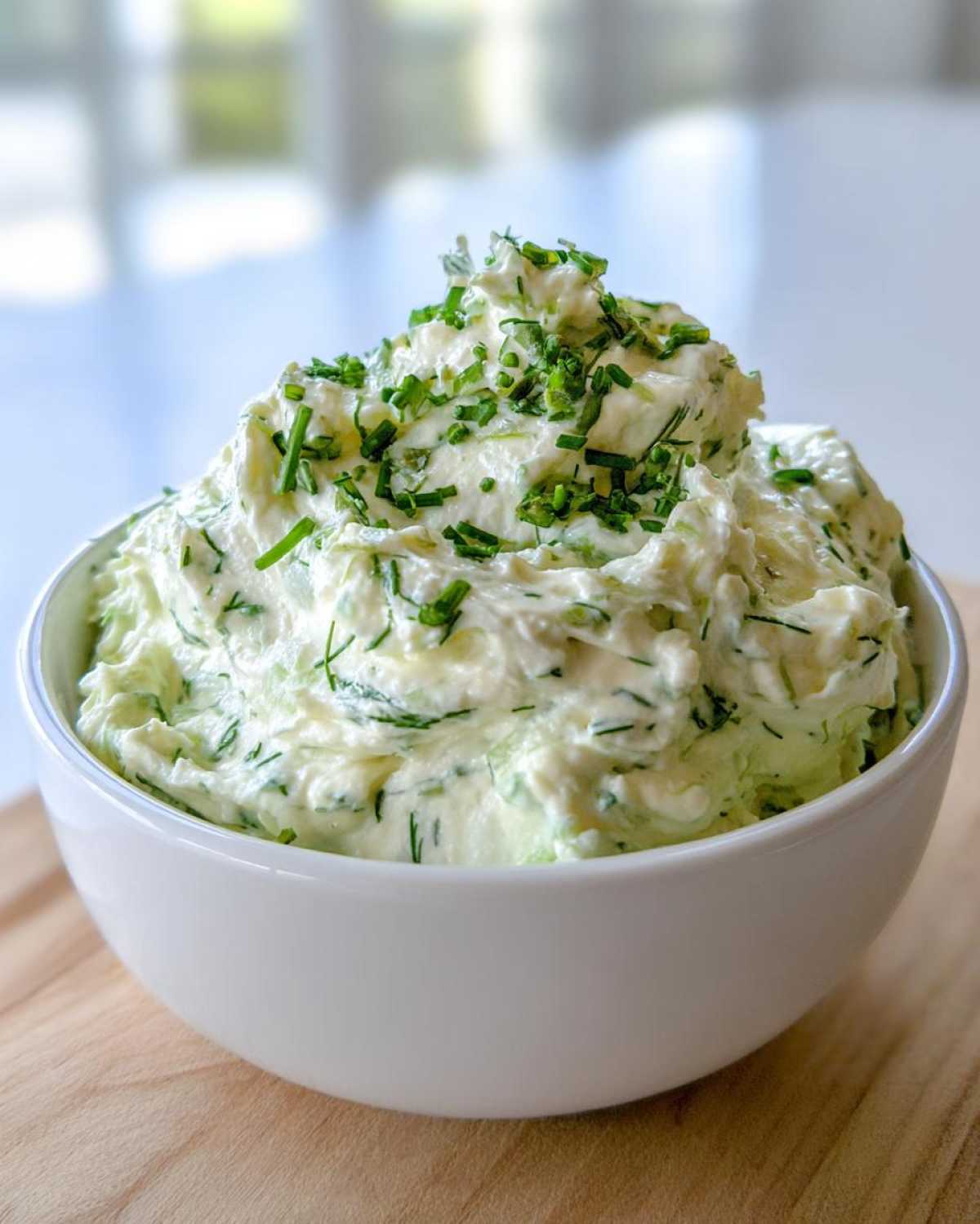 A white bowl filled high with creamy, green-flecked pickle dip, generously garnished with fresh chopped chives.