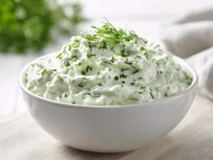 A creamy white bowl filled with vibrant green pickle dip, topped with fresh dill.