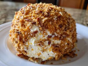 A close-up of a creamy pineapple cheese ball coated entirely in toasted pecans and coconut flakes.