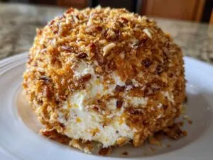 A close-up of a creamy pineapple cheese ball coated entirely in toasted pecans and coconut flakes.