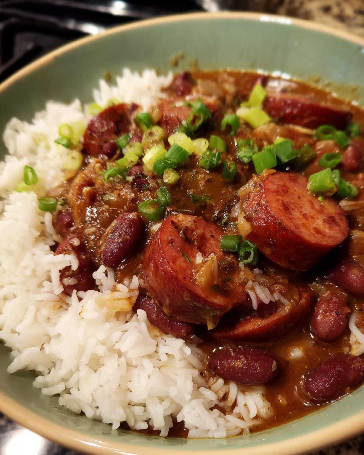 A close-up bowl of amazing red beans and rice topped with sliced smoked sausage and green onions.