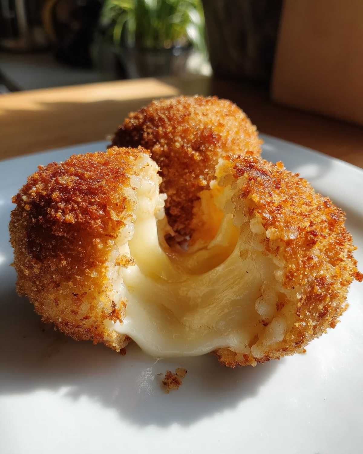 Close-up of crispy fried rice balls, one broken open revealing melted, gooey cheese inside.
