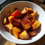 Close-up of beautifully caramelized, roasted sweet potato chunks served in a white bowl.