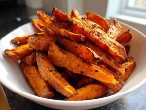 Close-up of a white bowl filled with crispy, seasoned roasted sweet potato wedges.