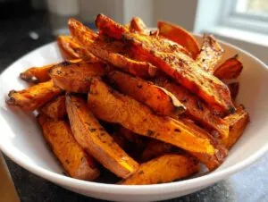 Close-up of a white bowl filled with crispy, seasoned roasted sweet potato wedges.