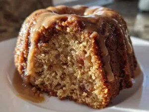 Close-up of a moist slice of apple bundt cake topped with rich caramel glaze dripping down the sides.