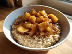 Close-up of a white bowl filled with creamy apple cinnamon oatmeal, topped generously with caramelized, spiced apple chunks.