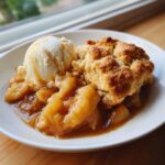 A warm serving of apple cobbler recipe topped with a scoop of vanilla ice cream and caramel drizzle.