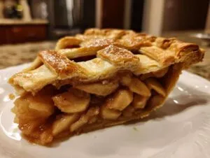 Close-up of a thick slice of apple pie recipe showing flaky lattice crust and cinnamon-spiced apple filling.