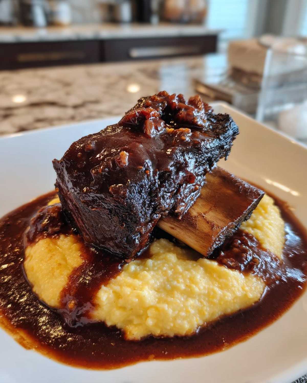 A single portion of rich, dark braised short ribs served over creamy yellow polenta with excess sauce.