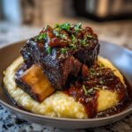 A single, perfectly cooked braised short ribs served over creamy polenta, topped with rich sauce and fresh herbs.
