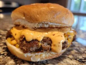 Close-up of a juicy burger patty topped with melted cheese and generous amounts of homemade Big Mac sauce on a soft bun.