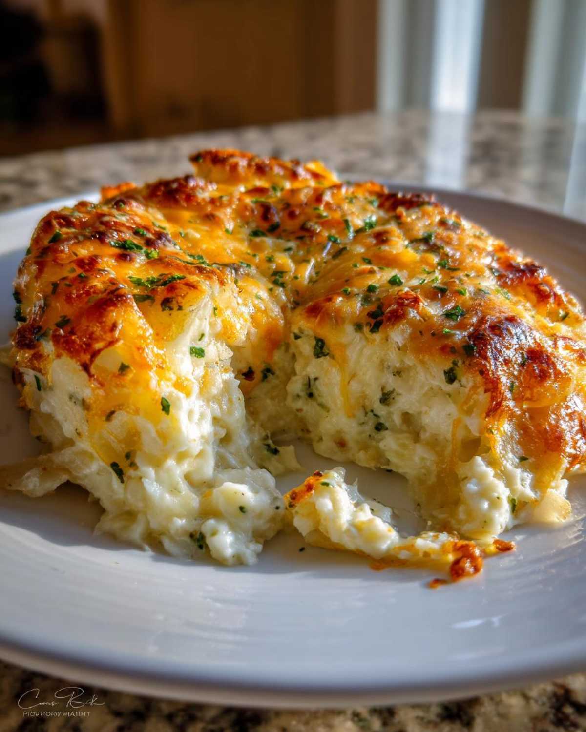A scoop taken out of a rich, cheesy potato casserole topped with melted, browned cheese and parsley.
