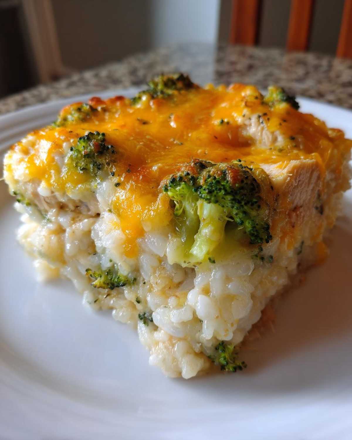 A close-up of a square serving of creamy chicken broccoli rice casserole topped with melted cheddar cheese.