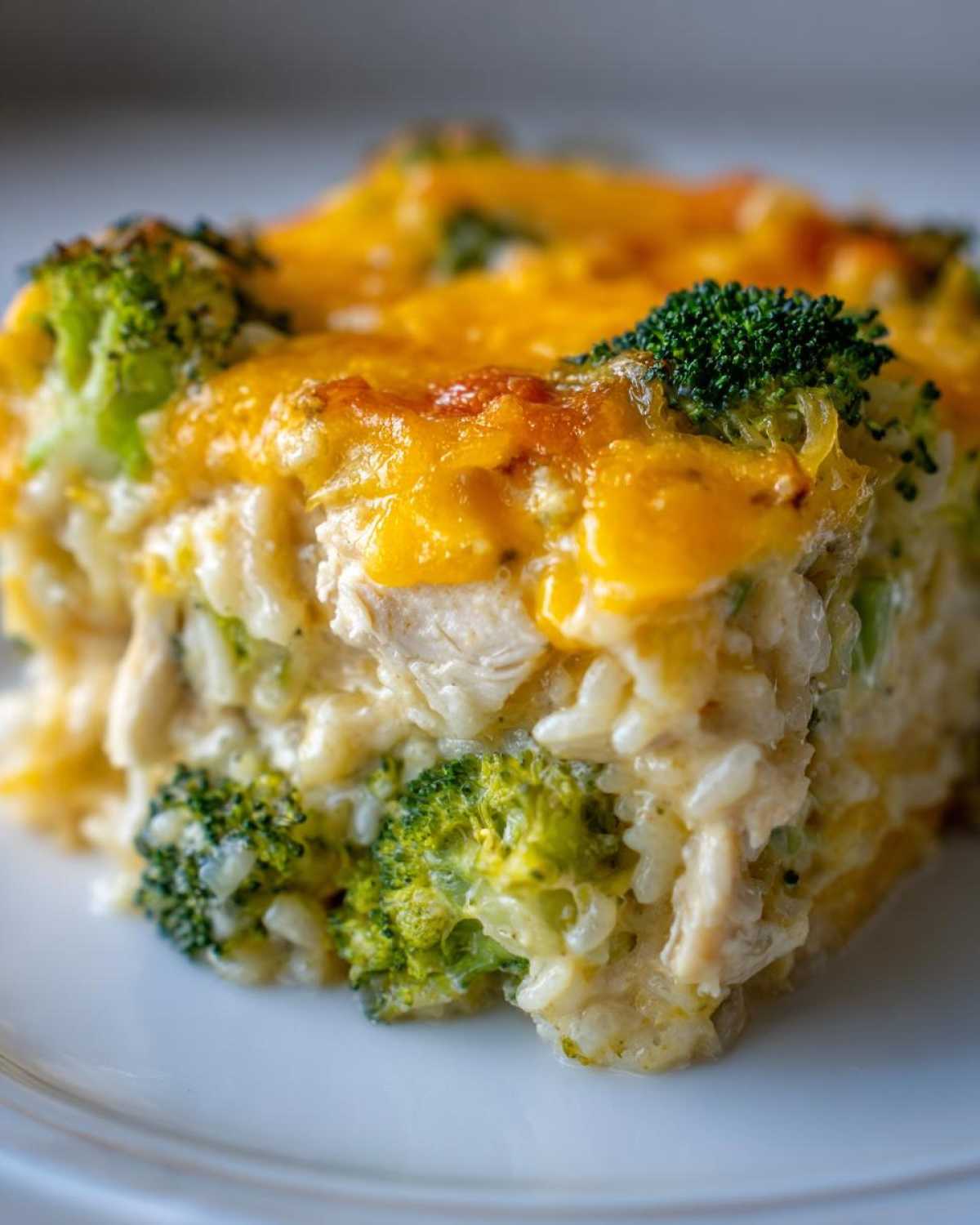 A close-up serving of creamy chicken broccoli rice casserole topped with melted cheddar cheese.