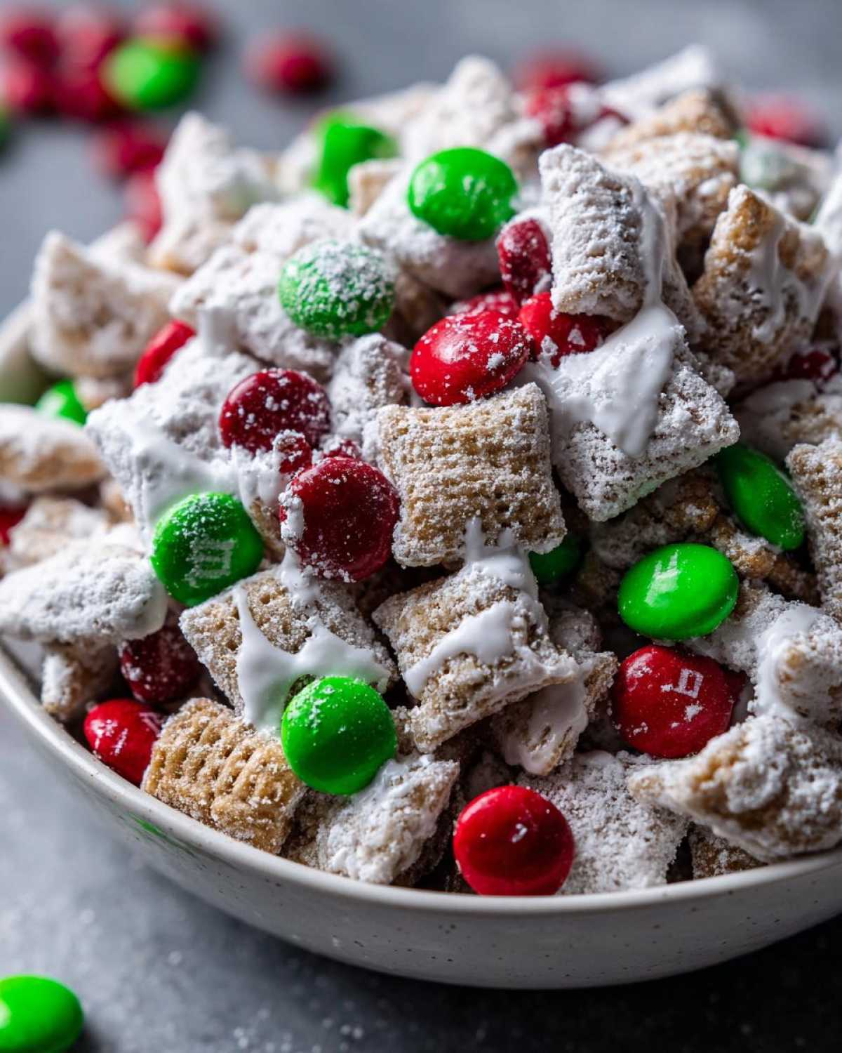 A close-up of Christmas puppy chow coated in powdered sugar, mixed with red and green M&Ms, ready to serve.