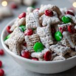 Close-up of delicious Christmas puppy chow coated in powdered sugar and drizzled with icing, mixed with red and green M&Ms.