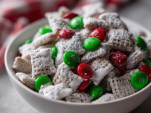 Close-up of Christmas puppy chow coated in powdered sugar with red and green M&Ms in a white bowl.