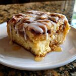 A close-up of a single serving of cinnamon roll apple pie drizzled with white icing.