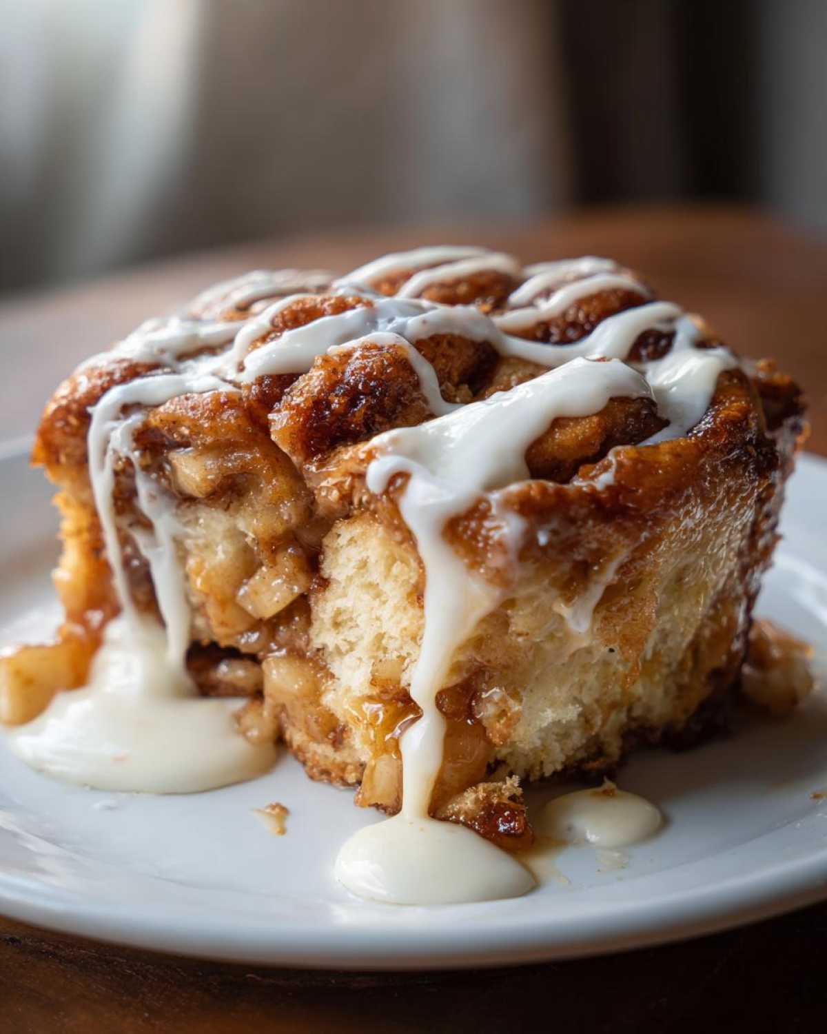 A close-up of a decadent cinnamon roll apple pie slice topped with thick white icing dripping down the sides.