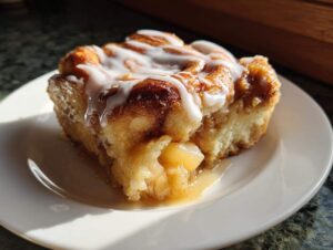 A close-up of a gooey slice of cinnamon roll apple pie topped with white icing.