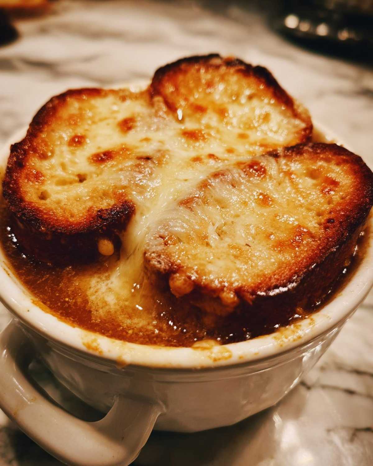 Close-up of a piping hot bowl of french onion soup topped with toasted bread and bubbling, melted Gruyère cheese.