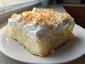A moist slice of coconut poke cake topped with fluffy white frosting and toasted coconut flakes.