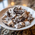 A close-up of homemade cookies and cream puppy chow heavily dusted with powdered sugar and mixed with crushed chocolate sandwich cookies.
