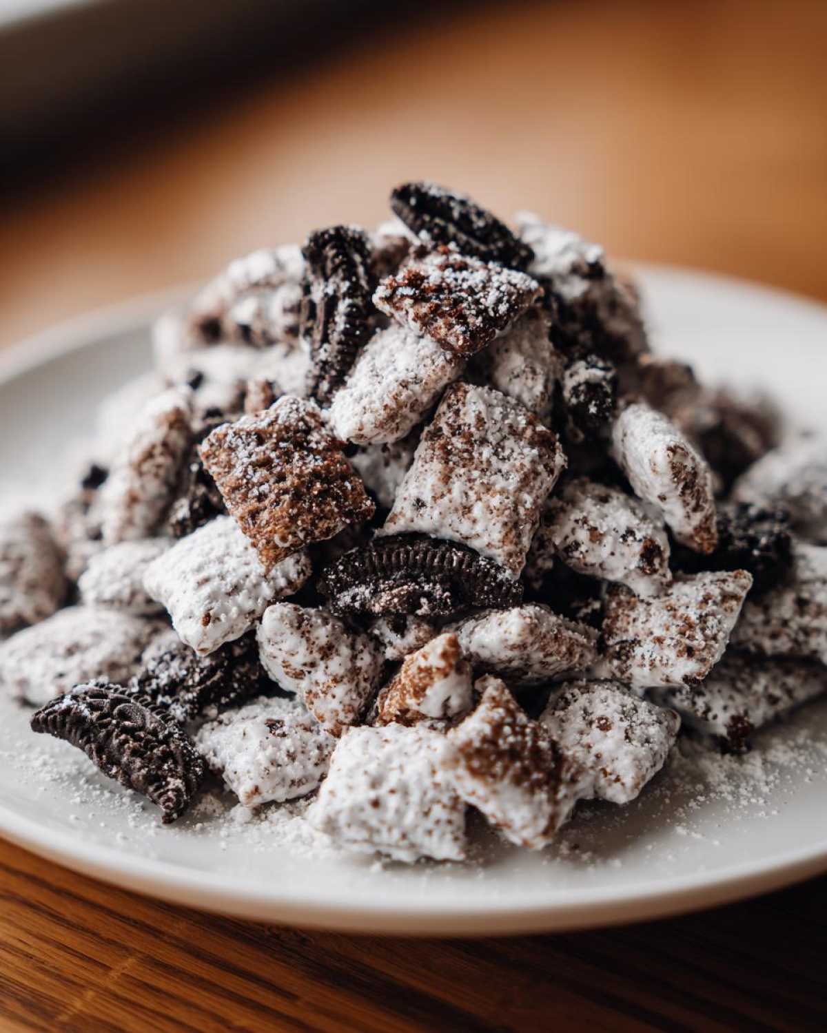 A close-up of a mound of cookies and cream puppy chow coated in powdered sugar on a white plate.