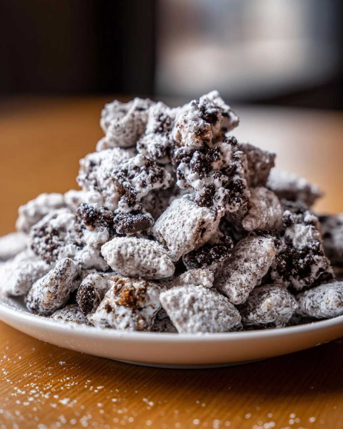 A generous pile of cookies and cream puppy chow coated heavily in powdered sugar on a white plate.